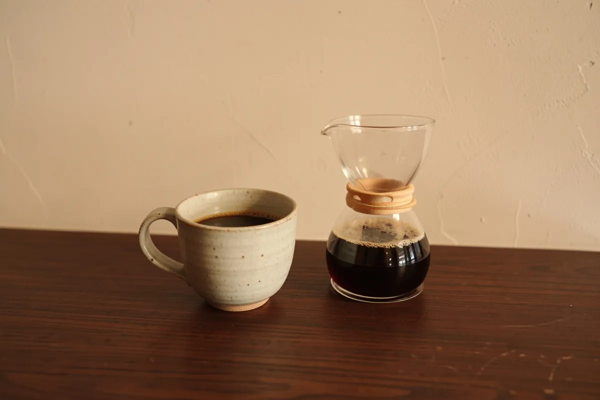 A cup of drip coffee and a glass server on a dark wooden counter